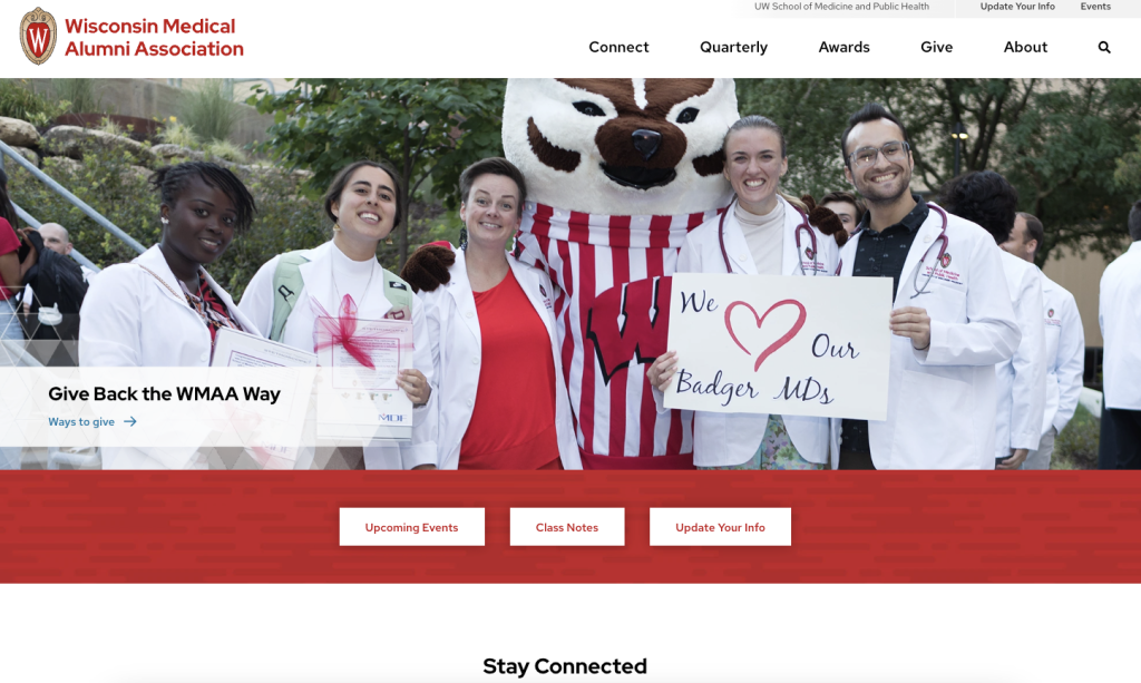 Home page of WMAA web site featuring menu navigation at the top of the page, a banner image showing five medical students wearing white coats and two wearing stethoscopes around their necks next to the Bucky Badger mascot and holding a sign saying "we love our Badger MDs,." Additional menu buttons in the middle of the page say "Upcoming Events," "Class Notes," and "Update Your Info."